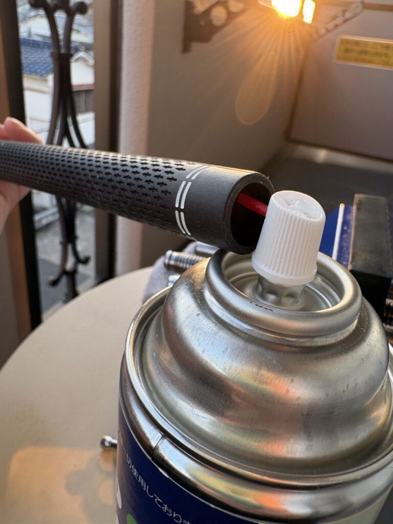 新しいゴルフグリップの内部に、交換用溶剤スプレーのノズルを差し込み、たっぷりと噴射している様子