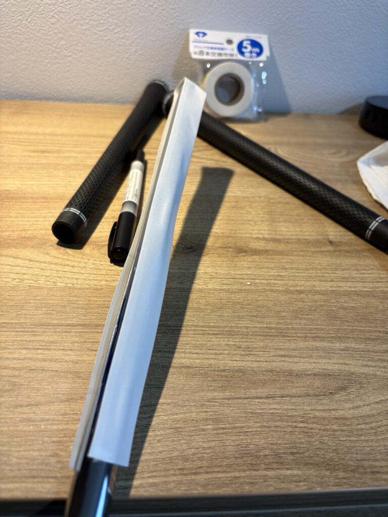 ゴルフクラブのシャフトに新しいグリップ交換用両面テープを縦貼りで貼り付けている様子