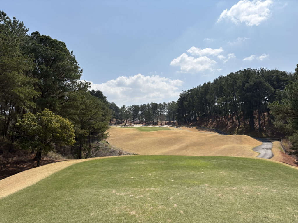 有馬ロイヤルゴルフクラブ ノーブルコース18番ホールのパー5。ティーイングエリアから、連なるマウンドと多数の白いバンカー、右手の崖、遠くのグリーンへと続く戦略的な景色。