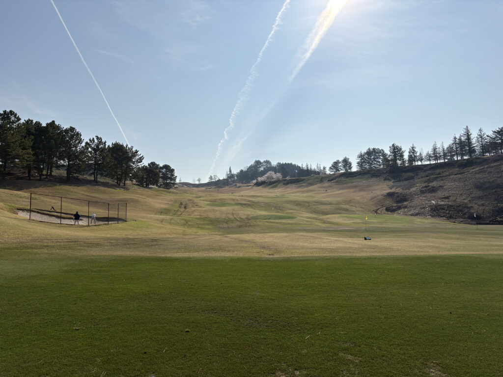 有馬ロイヤルゴルフクラブ ノーブルコースの、広大でネットがない開放的なゴルフ練習場。遠くにバンカーや目標のフラッグが見える。