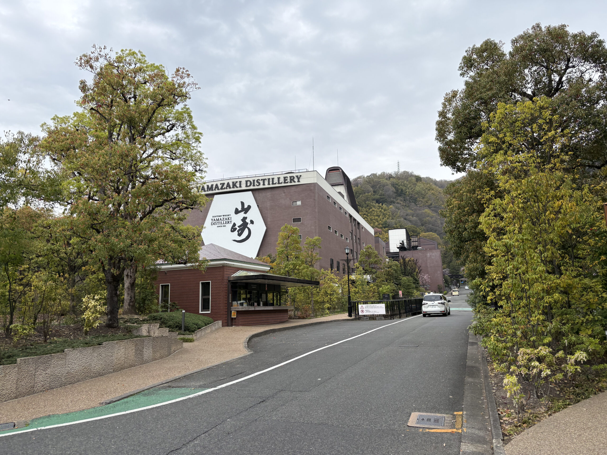 サントリー山崎蒸溜所の外観。白い大きなロゴが描かれた茶色の建物と周囲の緑。