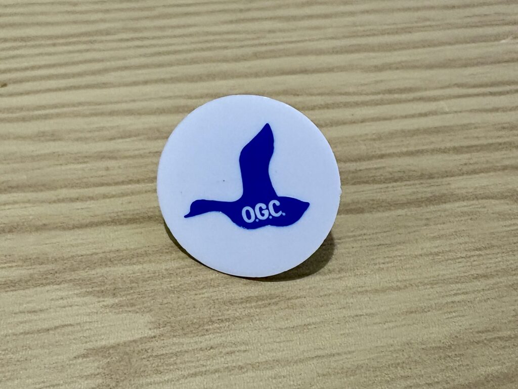 兵庫県の名門、小野ゴルフ倶楽部のプラスチック製マーカー。白地に青色で鴨のシルエットと「O.G.C.」の文字がデザインされている。